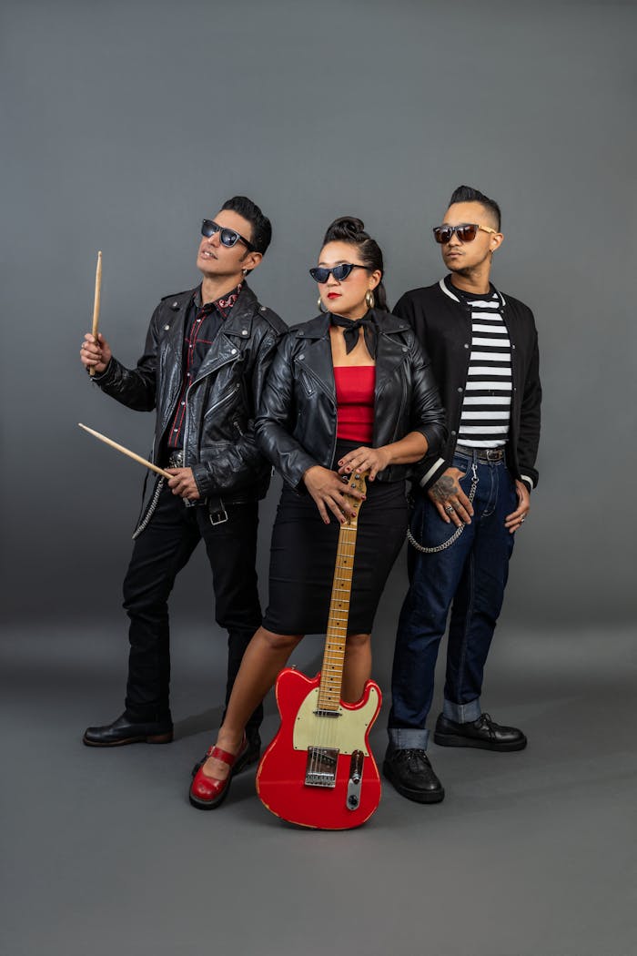 Fashionable band members posing with musical instruments in studio setting.